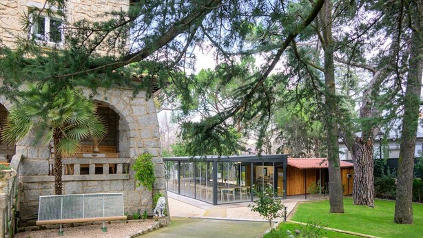 A courtyard with a stone building, a glass-enclosed dining area, and a wooden structure.