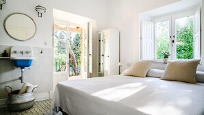 A bedroom with a bed, a round mirror, a blue sink, and a window with a view of greenery.