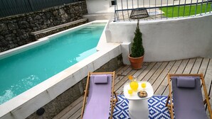 Un espace aménagé au bord de la piscine, avec deux chaises longues, une table sur laquelle se trouve une carafe de jus d’orange et une petite plante en pot.
