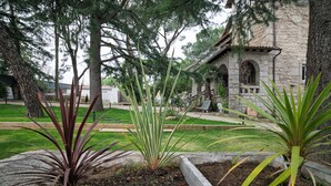 Un jardin aménagé avec différentes espèces de plantes et, au fond, un bâtiment en pierre doté d’arcades.