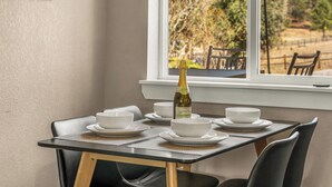 A dining table set with white bowls and plates, a bottle of wine, and a view of trees and a fence through a window. - LUX Guest Suite Near Amazing Hiking Trails (Colorado Springs)