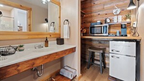 Un baño moderno con un tocador de madera, un espejo grande, un lavamanos y un microondas integrado.