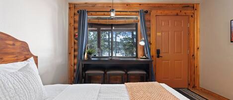 Une chambre à coucher avec un lit, un bureau avec des chaises, une fenêtre avec des rideaux et une porte.