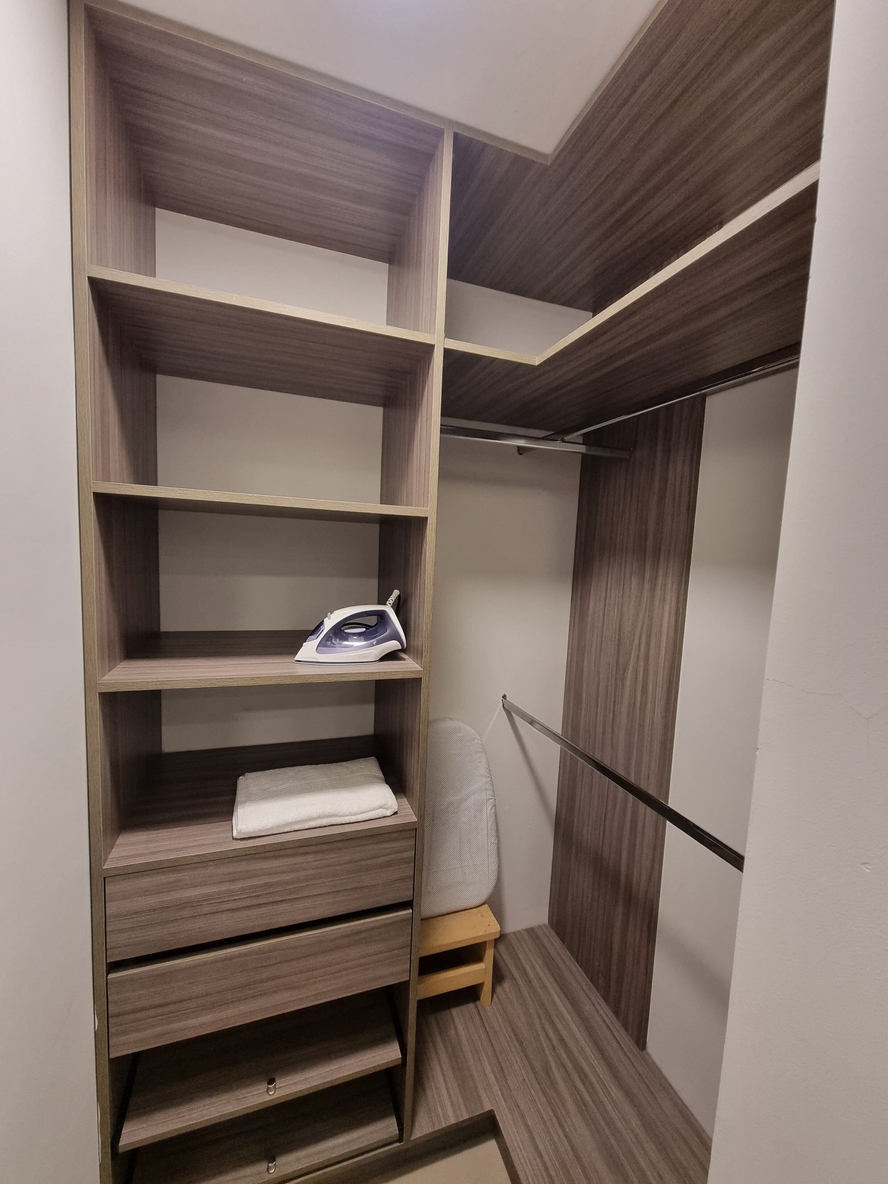A walk-in closet with wooden shelving, a hanging rod, and a small ironing station.