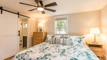 A bedroom with a bed, a ceiling fan, a nightstand, a lamp, a window, and a door.