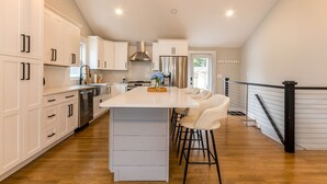 Una cocina moderna con armarios blancos, electrodomésticos de acero inoxidable y una isla central con taburetes de bar.