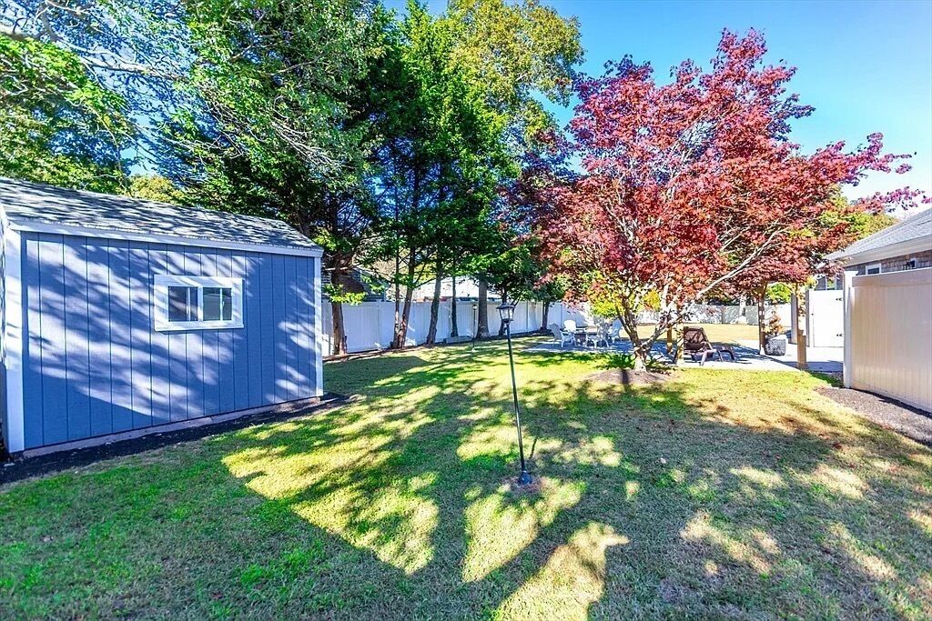Un jardin avec un abri de jardin, un arbre aux feuilles rouges et une pelouse.
