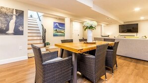 Una sala de estar moderna con una mesa de comedor de madera, sillas de mimbre, un televisor grande y obras de arte en las paredes.