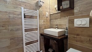 A bathroom with a wooden floor, a white toilet, a sink with a mirror above it, and a towel rack.