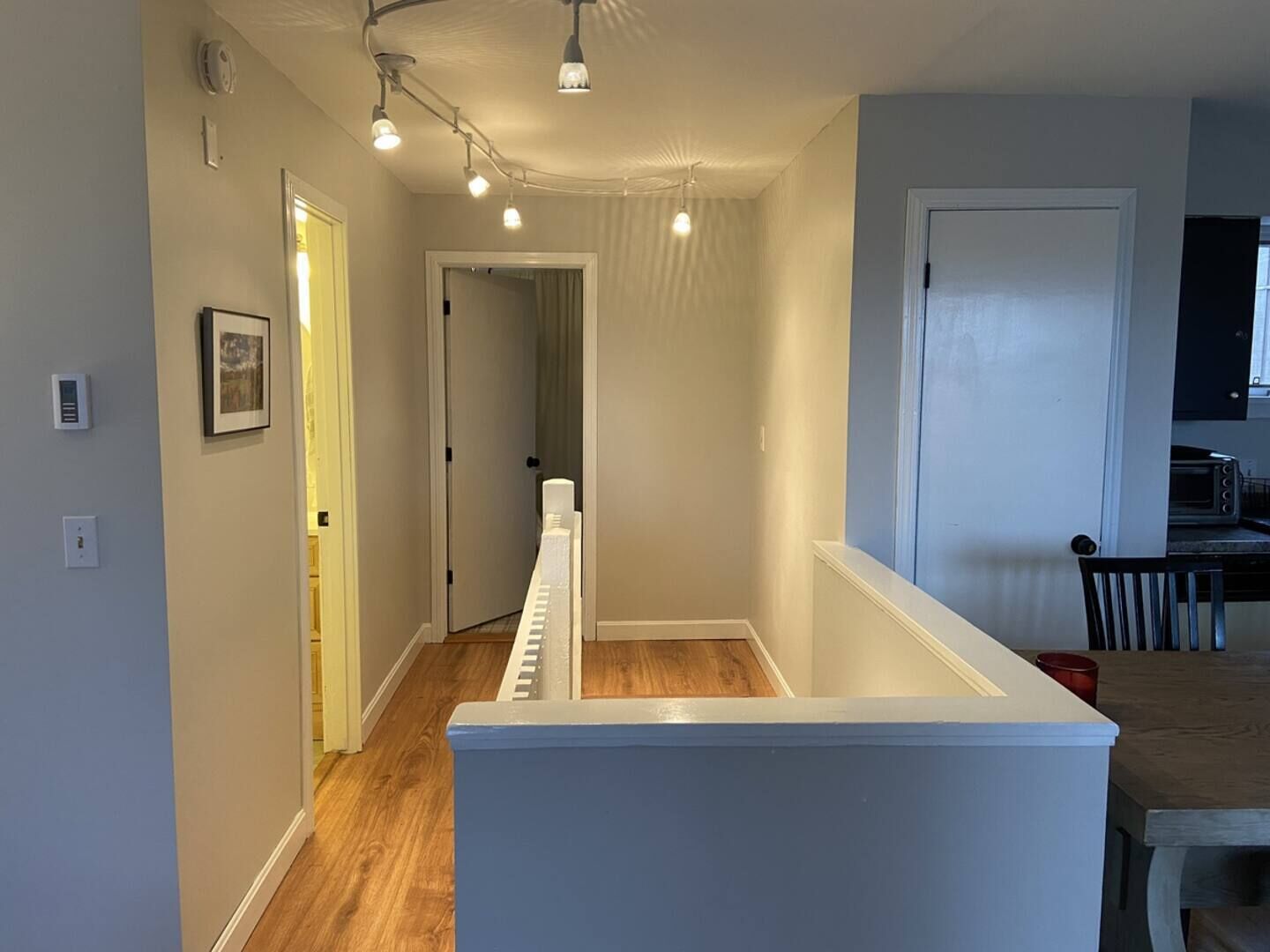 A narrow hallway with a white bench, a door leading to another room, and a kitchen area with a dining table and chairs.