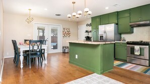 A modern kitchen with green cabinets, a central island, stainless steel appliances, and a dining area with wooden chairs and a table.