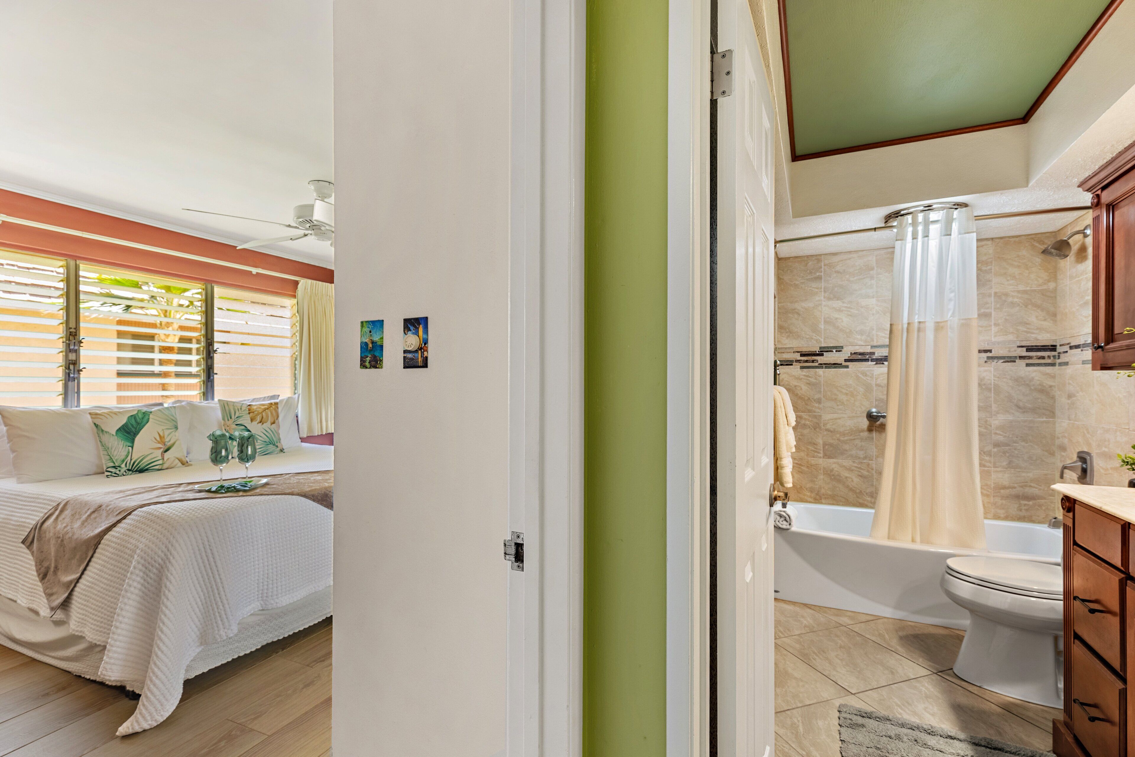 Un dormitorio con cama, ventana con persianas y vista al baño.
