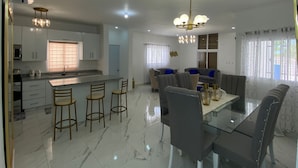 A modern kitchen with a central island, bar stools, a dining table with chairs, and a living area with a sofa and a coffee table. - Welcome  to Villa Julesmi  (La Romana)