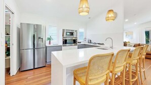Une cuisine moderne dotée d'un îlot central, d'appareils électroménagers en acier inoxydable, de chaises en osier et de luminaires suspendus.