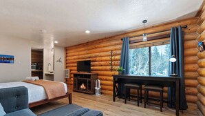 A log cabin room with a bed, a TV, a fireplace, and a dining area.