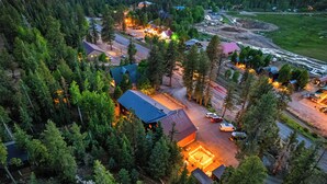 An aerial view of a forested area with a cluster of buildings, roads, and a lit-up area suggesting a gathering or event.