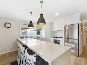 A modern kitchen with a central island, white cabinetry, stainless steel appliances, pendant lighting, and a clock on the wall.