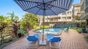 A poolside area with a pool, lounge chairs, and a striped umbrella.