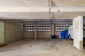 Un parking avec des murs en béton, un fourgon blanc garé à droite et une bâche bleue sur le sol.