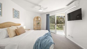 A hotel room with a bed, a ceiling fan, a TV, a wicker headboard, a wicker shelf, and a balcony with a view. - Surfside Beachfront 3bed Apt - Direct Beach Access (Buddina)
