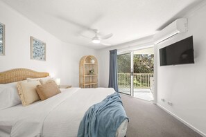 A hotel room with a bed, a ceiling fan, a TV, a wicker headboard, a wicker shelf, and a balcony with a view.