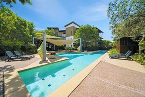 A swimming pool with lounge chairs, a shaded area, and a building in the background.