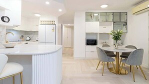 A modern kitchen with white cabinetry, a marble countertop, and a dining area with a round table and chairs.