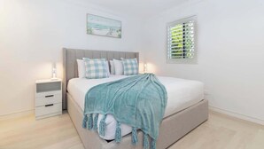 A bedroom with a bed, nightstands, a window with blinds, and a wall-mounted artwork.