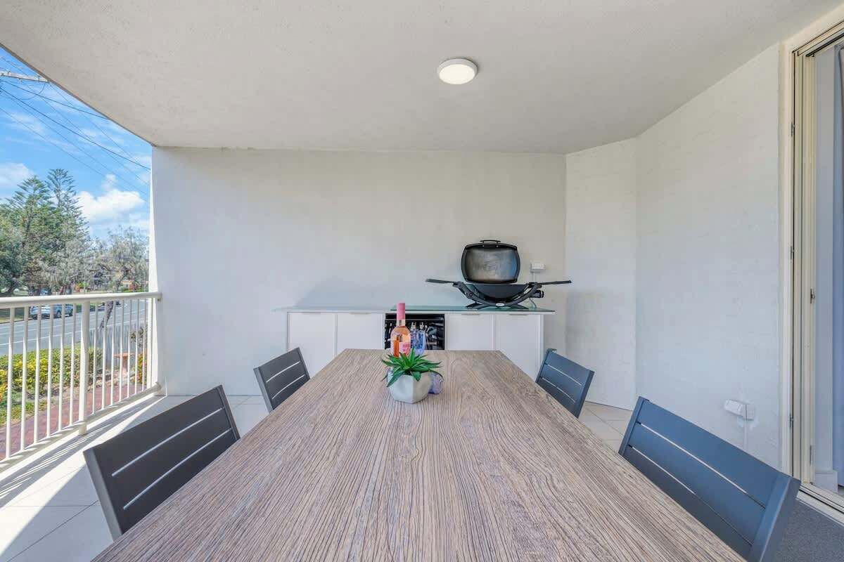 A balcony with a dining table, chairs, a potted plant, and a television.
