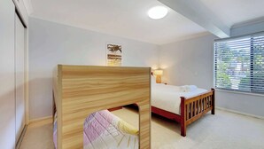 Un dormitorio con una cama litera, una cama individual, una lámpara de noche, una ventana con persianas y una luz en el techo.