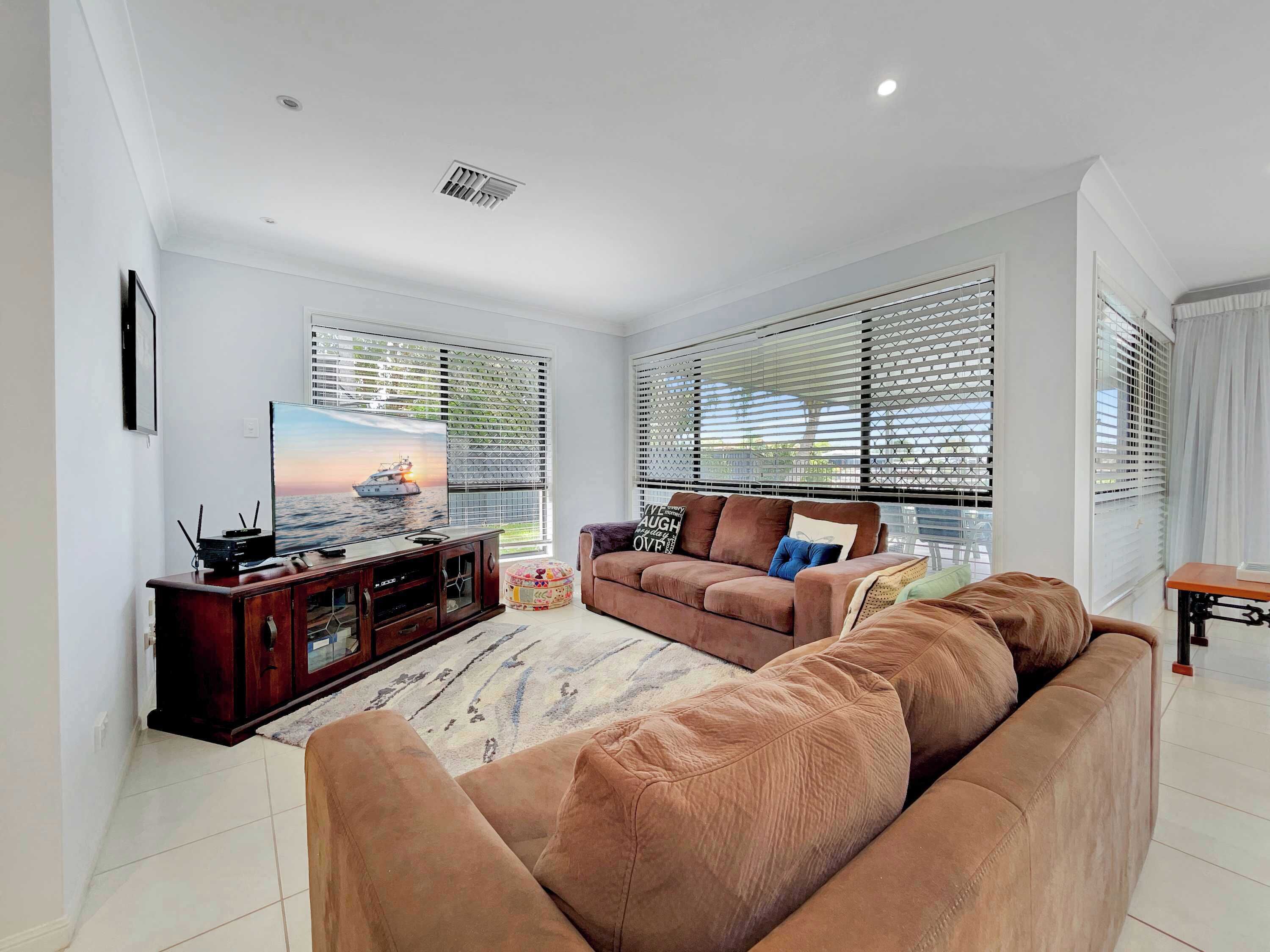 A living room with a large flat-screen TV, a brown sofa, and a wooden entertainment unit.