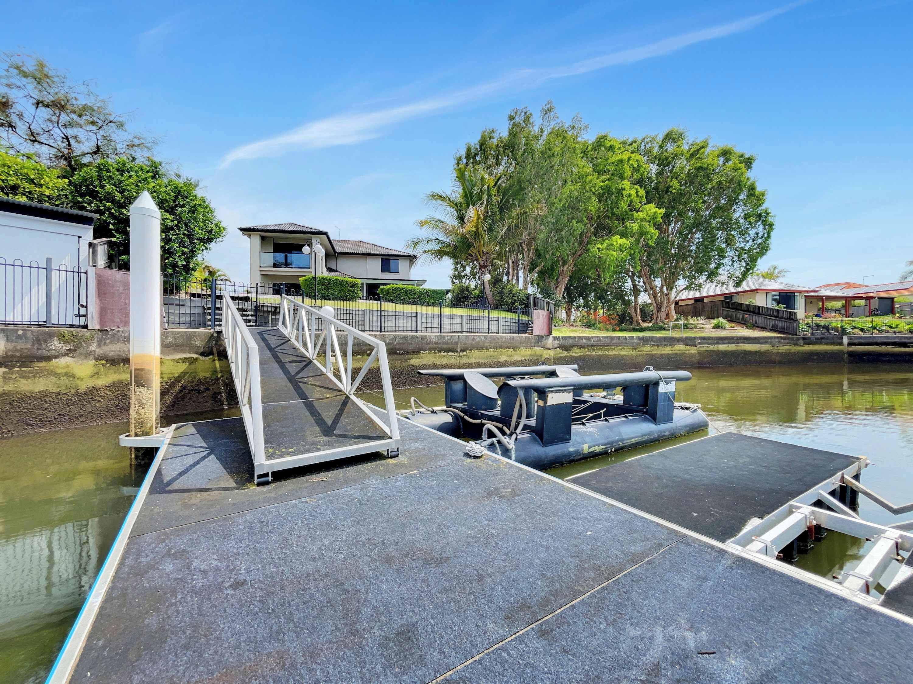 A dock with a bridge leading to a house, a boat, and a calm water body.