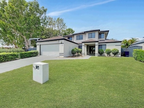 A two-story house with a garage, a well-maintained lawn, and a clear sky. - Spacious Family & Dog-Friendly Home on the Water (Banksia Beach)