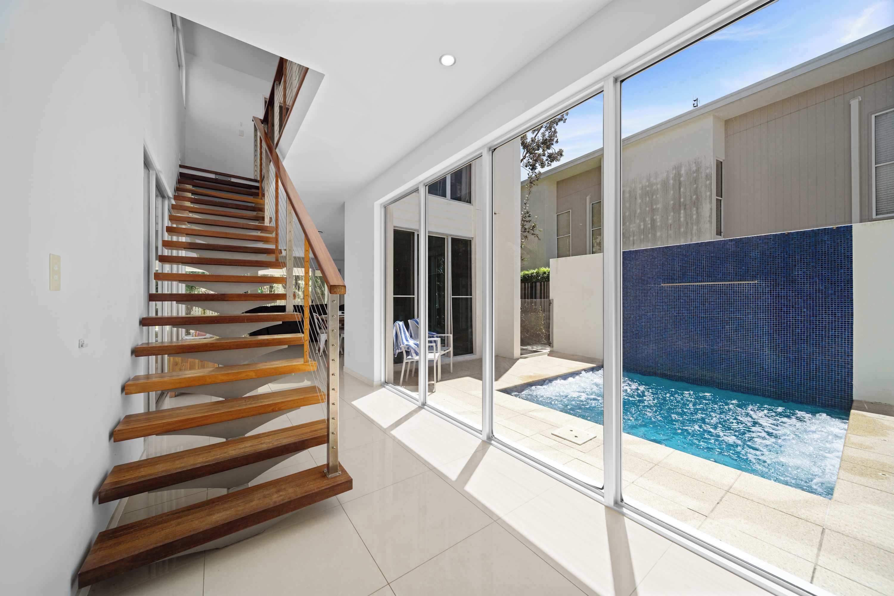 A modern interior with a wooden staircase, a glass door leading to a pool area, and a view of the outdoors.