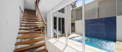 A modern interior with a wooden staircase, a glass door leading to a pool area, and a view of the outdoors.