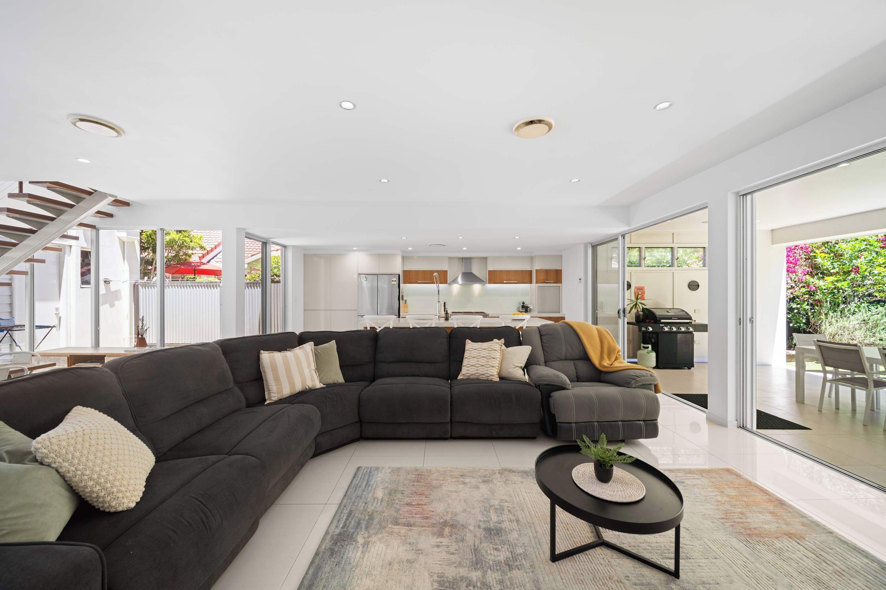 A modern living room with a sectional sofa, a coffee table, and a staircase leading to an upper level.