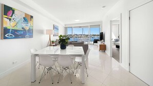 A modern living room with a dining area, large windows, and a view of the marina.