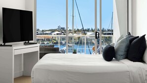 A modern hotel room with a bed, a TV, and a view of a marina.