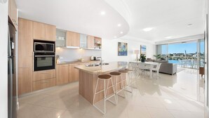 A modern kitchen with a central island, bar stools, and a dining area with a view.