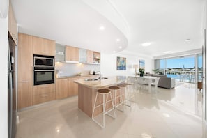 A modern kitchen with a central island, bar stools, and a dining area with a view.
