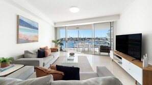 A modern living room with a large TV, a sofa, a coffee table, and a view of a marina through large glass doors.