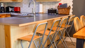A kitchen with a wooden island, metal chairs, a stainless steel sink, and a red appliance.