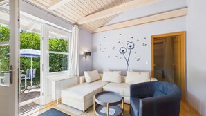 Een moderne woonkamer met een bank, een ronde salontafel en een blauwe fauteuil. Er is een groot raam met gordijnen, een wandlamp en een decoratieve muurstickers.