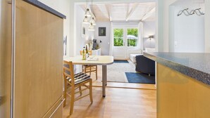 Een moderne keuken met houten kasten, een eethoek met een tafel en stoelen, en uitzicht op het buitengebied door een deur.