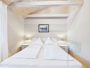 Ein Schlafzimmer mit einem Doppelbett, zwei Nachttischen, einem gerahmten Bild an der Wand und einer Holzbalkendecke.