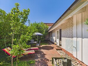A patio with a table and chairs, a small tree, and a brick pathway leading to a building.