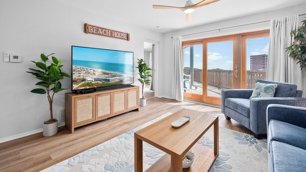 A modern living room with a flat-screen TV, wooden cabinet, blue sofa, and a ceiling fan.