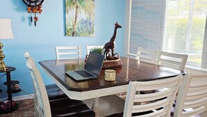 Un'area pranzo con un tavolo di legno, sedie bianche, un portatile, una statuetta di giraffa e un orologio a parete.