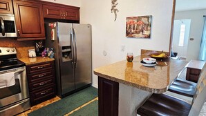 Cucina con isola centrale, elettrodomestici in acciaio inossidabile e zona pranzo con una sedia.