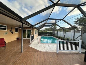 A covered outdoor area with a pool, wooden flooring, and a red chair. - Family friendly 3bed, 2bath house with WiFi, AC, Pool. 6mi-beach, 13mi-airport (Pembroke Pines)